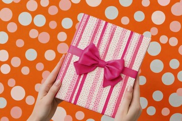 Festive gift box with bow held in hands against colorful polka dot background