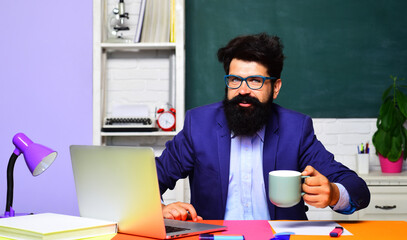 Smiling male teacher or university professor sitting at desk in classroom and having coffee break....