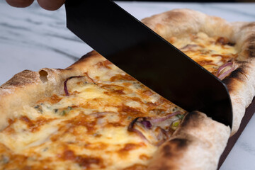 Gastronomy. Caucasian male hand holding a black kitchen knife, slicing a mozzarella, provolone and...