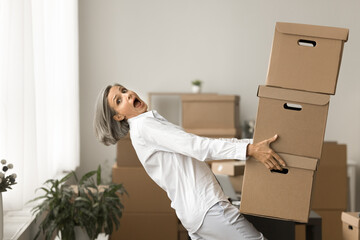 Overwhelmed mature business woman carrying bending stack of heavy boxes with fragile products about...