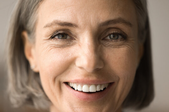Close up portrait of happy mature grey haired woman with natural makeup, healthy white teeth looking at camera with toothy smile, laughing. Pretty senior lady face shot