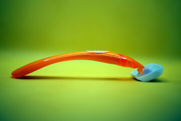 A vibrant orange and white razor placed on a soft yellow surface