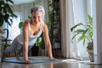 Happy smiling mature middle-aged woman with gray hair does plank exercise. Anti aging concept