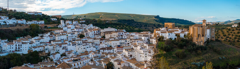 Setenil de las Bodegas in Spain features houses built into cliffs, whitewashed buildings, terracotta roofs, and a large church amidst rolling hills.