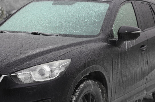 The car was iced over in winter after an icy rain. The windshield was covered with ice. Frost, rain and a car. Blurred background