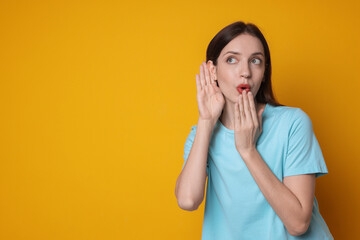 Woman showing hand to ear gesture on orange background, space for text