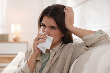 Young woman with tissue blowing runny nose at home