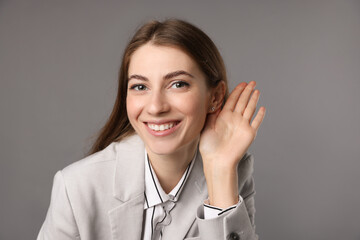 Woman showing hand to ear gesture on grey background