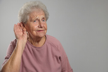 Senior woman showing hand to ear gesture on grey background, space for text