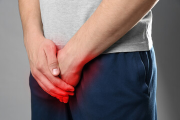 STD (sexually transmitted diseases). Man holding hands near his groin on grey background, closeup
