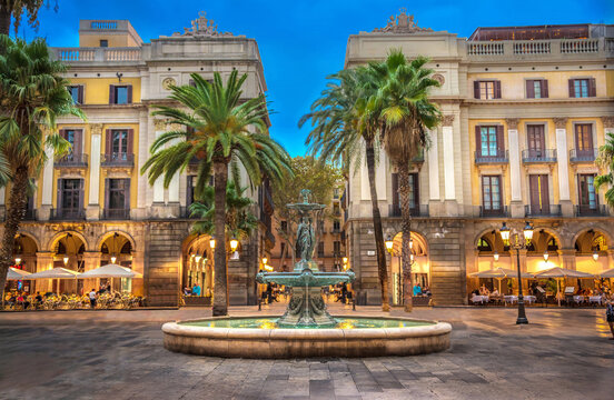 Diners enjoy the peaceful setting, flowing fountain and palm trees of the Pla&ccedil;a Reial (Royal Square) at blue hour on a summer evening in Barcelona, Spain.