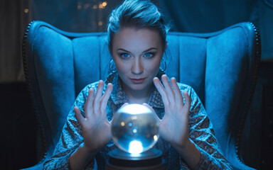 水晶玉を見つめる西洋の占い師： 薄暗い部屋で水晶玉を見つめる占い師。青い瞳の占い師の顔に神秘的な表情が浮かぶ。	