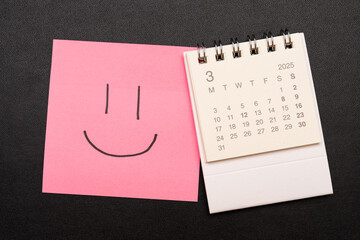 Simple desk calendar for MARCH 2025 with smiling face on sticky note. Calendar concept with copy...