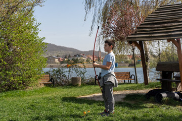 Boy practicing archery with toy bow and arrow by the lake in green park on sunny day. Concept of...
