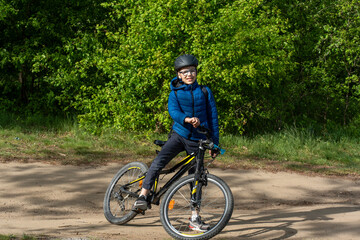 Fototapeta premium Young boy wearing a helmet posing with his bicycle on sunny day in the forest, surrounded by greenery. Concept of outdoor activities, healthy lifestyle, and cycling adventure. High quality photo