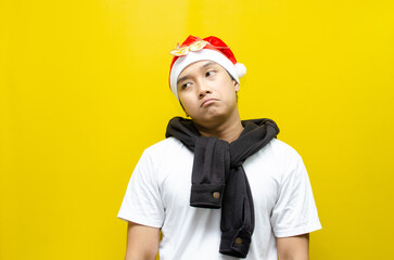 Thoughtful Young Asian Man in Santa Hat and Scarf Celebrating Christmas with a Sad Expression, Deep...