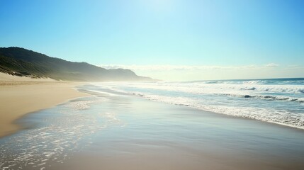 Serene Coastal Scene with Gentle Waves at a Tranquil Beach Under Clear Blue Sky and Lush Green Mountains in Background Illuminated by Bright Sunshine