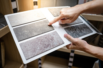 Flooring material design collection. Designer hand pointing at stone tile sample on display catalog. Customer choosing rough texture and pattern for floor finishing at home design store