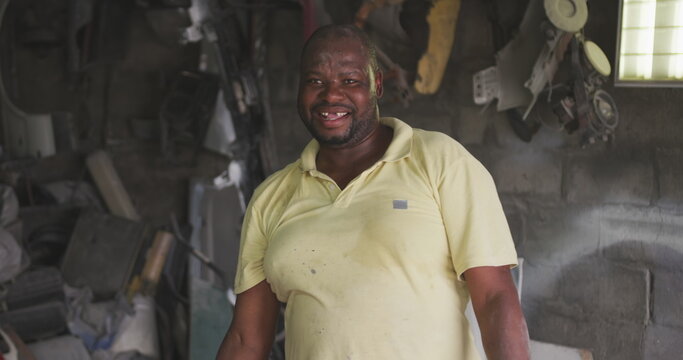 Portrait of a happy African handyman in a township workshop, looking at camera and smiling, slow mot