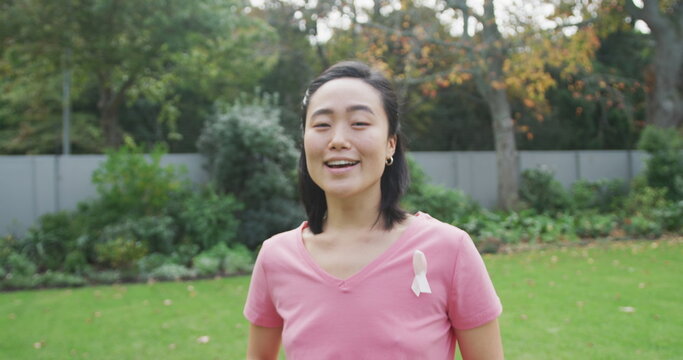 Portrait of happy asian woman wearing pink t shirt and cancer ribbon, standing in garden laughing