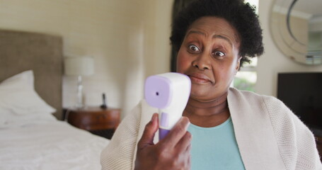 African american senior woman measuring her temperature while sitting on the bed at home