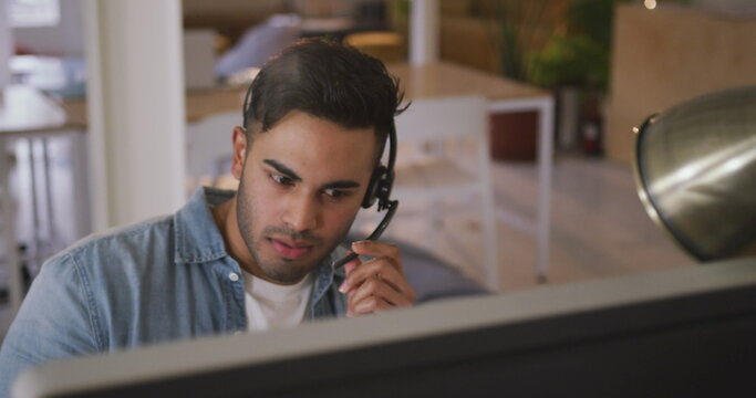 Front view of a happy biracial man working in a creative office, wearing headset, talking and smilin