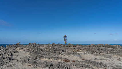 A man stands on the rocky volcanic coast of the island, smiling. Clothes are fluttering in the...
