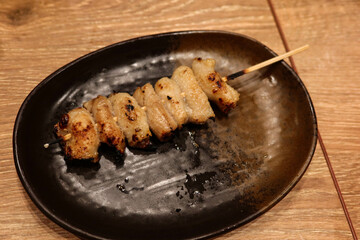 close up of grilled roasted Japanese chicken soft bone skewer on a black plate in a izakaya...