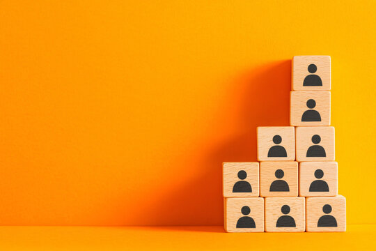 Stacked wooden blocks with black human icons on a vibrant orange background, illustrating teamwork, organization, and growth concepts.