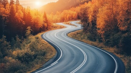 Naklejka premium Winding asphalt road through autumn forest, sunlit. Perfect for travel, adventure, and fall season themes; evokes journey and freedom.
