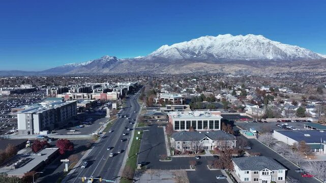 Aerial State highway traffic business Mt Timpanogos sn. Orem city, variety of stores businesses. Urban economy Malls, stores, residential neighborhoods, parks. High desert valley. Snow covered winter.
