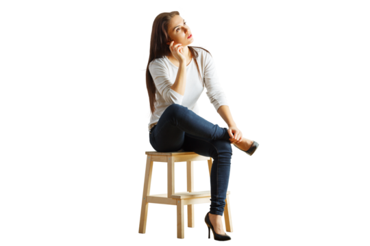 Woman seated on a wooden stool, dressed casually in a white top and jeans, looking thoughtful. Isolated on a clean white background, concept of contemplation
