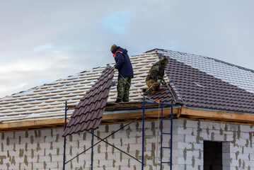 Two men are working on a roof, one of them is wearing a blue jacket