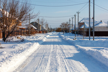 A snowy street with a few houses in the background