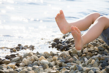 Close-up of children's feet above water on small pebbles on the beach. Summer vacation