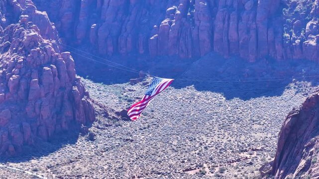 Aerial USA flag between mountains Utah slide. American USA flag between two red rock mountains. Celebration of Veterans Day in Southwestern desert Utah. Snow Canyon Park. Patriotic display of huge fla