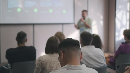 Speaker delivers a presentation to a group of attendees in a seminar. The audience is focused on the projected screen, capturing a learning atmosphere.