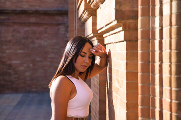 Fototapeta premium pretty young brunette woman rests her head on her arm on the wall and looks down. The woman is sad and depressed and feels pain and despair. She feels bad and negative, she is going to start crying.
