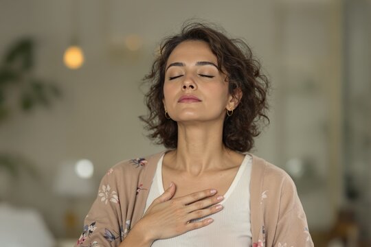 Mindful Woman Practicing Breathing Exercise for Relaxation, Portrait of a serene woman with closed eyes, hand on chest, engaging in a deep breathing exercise to find peace and mindfulness