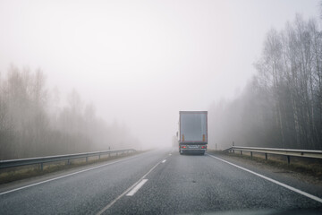  A truck driving on a foggy highway surrounded by bare trees, creating a serene and mysterious...