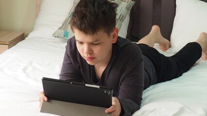 Smiling teenage school kid using tablet computer, relaxing on sofa at home, watching learning video, movie, online class, listening to music, communicates with friends, social networks