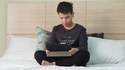 Smiling teenage school kid using tablet computer, relaxing on sofa at home, watching learning video, movie, online class, listening to music, communicates with friends, social networks