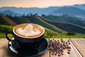 Latte art coffee in black ceramic cup with roasted coffee beans and mountain farming background. Concept for EU Deforestation or EUDR, regulation environmental policy and drinking coffee in European