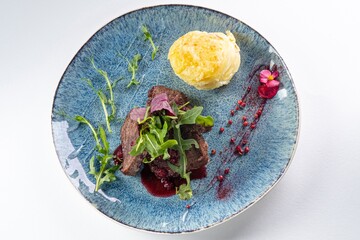 Beef Medallions with Arugula, Mashed Potatoes, and Sauce on a Plate Against a White Background