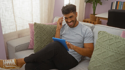 Young hispanic man smiling while using a tablet in a comfortable living room setting
