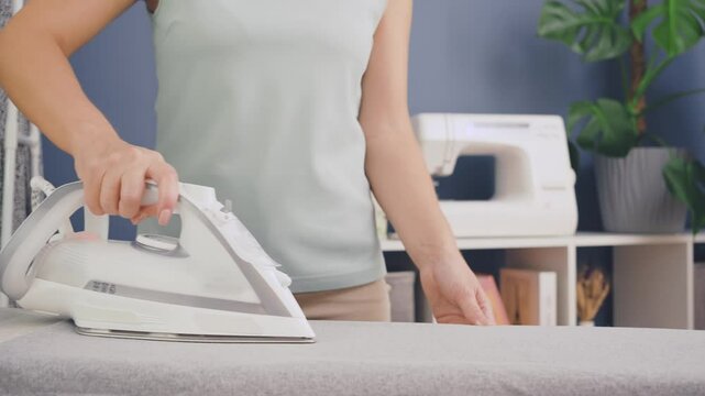 A woman irons a gray cloth on an ironing board in a home interior. 4k video. mid shot. Side view