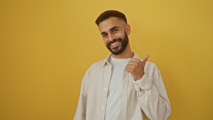 Obraz premium Young hispanic man giving thumbs up against isolated yellow background, smiling with a beard, wearing a casual shirt, and looking confident.