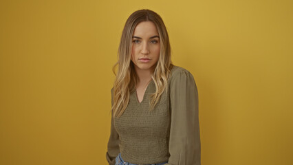 Obraz premium A young, attractive blonde woman stands against an isolated yellow background wall, showcasing a serene and confident expression.