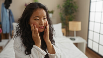 Beautiful young chinese woman indoors touching face in bedroom at home