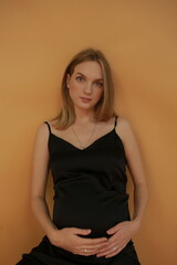 Obraz premium beautiful pregnant woman model in black dress on orange wall background. pregnant model in dress on yellow background sitting
